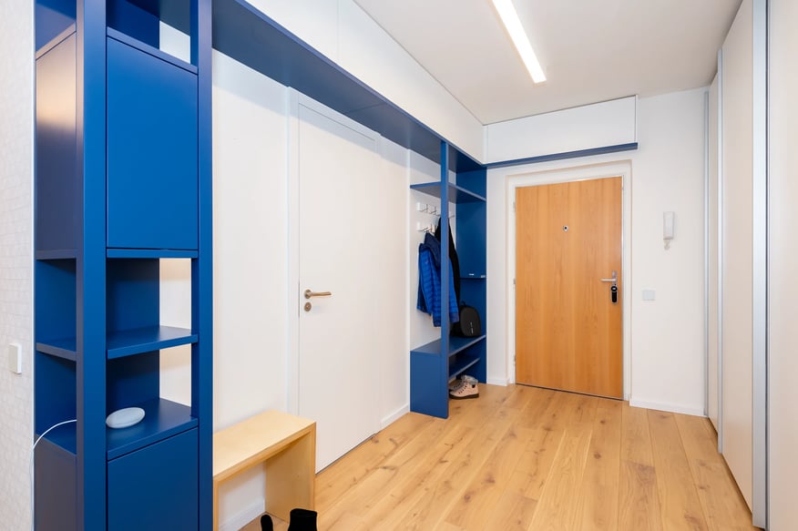 Moderní chodba s modrým nábytkem bílými dveřmi a dřevěnou podlahou.